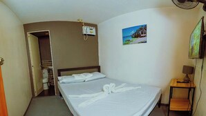 A hotel room with a bed, a small table with a lamp, a painting on the wall, and a fan on the ceiling. - Adventourist Inn Coron (Coron)