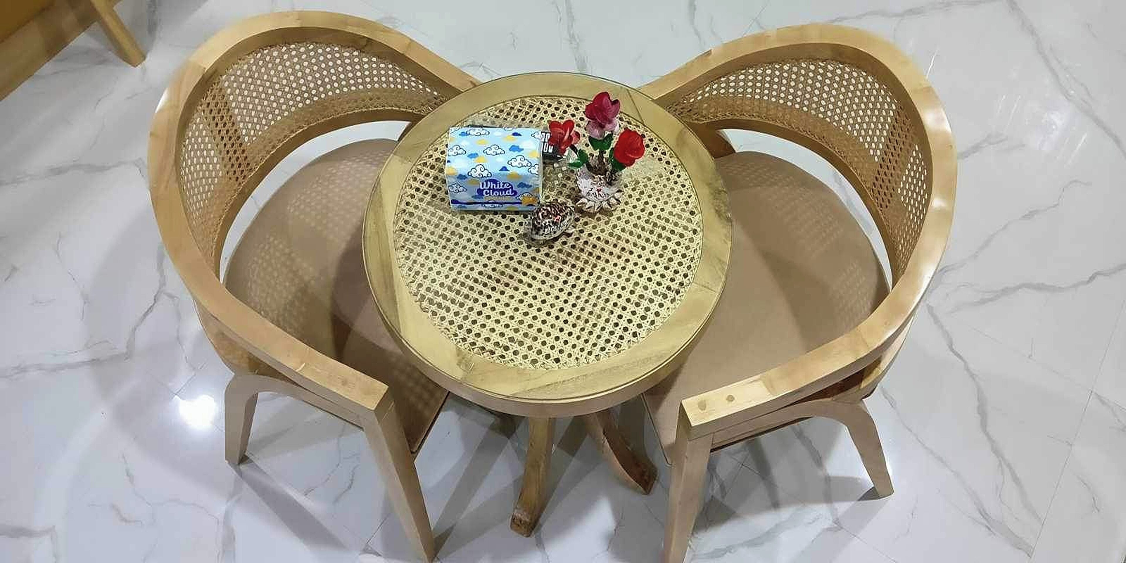 Una mesa redonda con superficie trenzada, rodeada por tres sillas de madera con respaldo perforado.