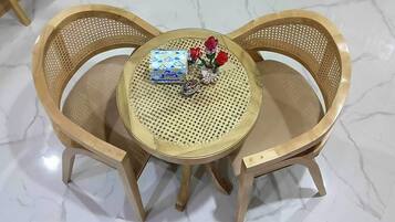 Una mesa redonda con superficie trenzada, rodeada por tres sillas de madera con respaldo perforado.
