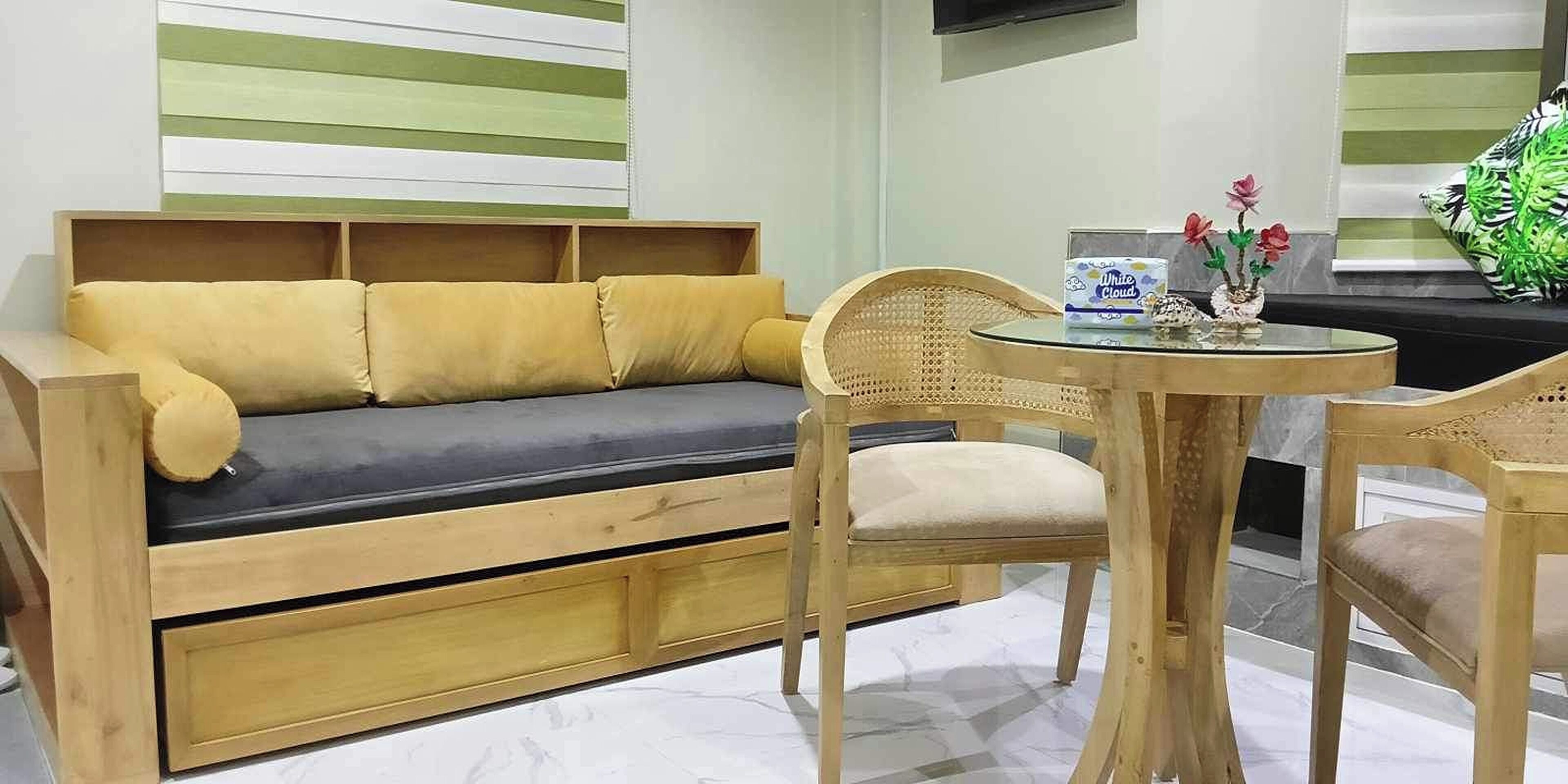 A wooden sofa with cushions, a round wooden table with chairs, and a decorative vase with flowers.