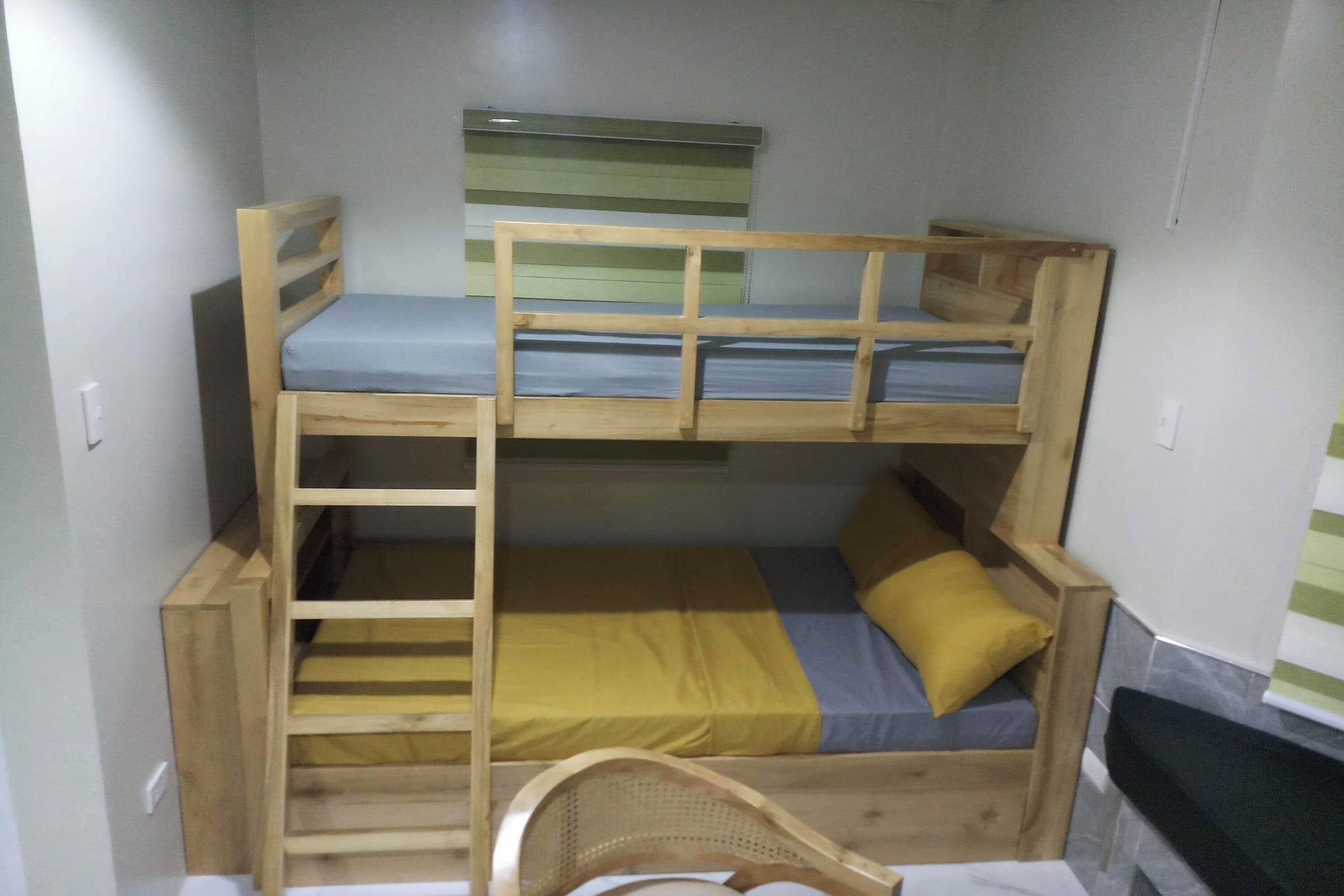 A bunk bed room with a wooden ladder, a small window, and a black chair.