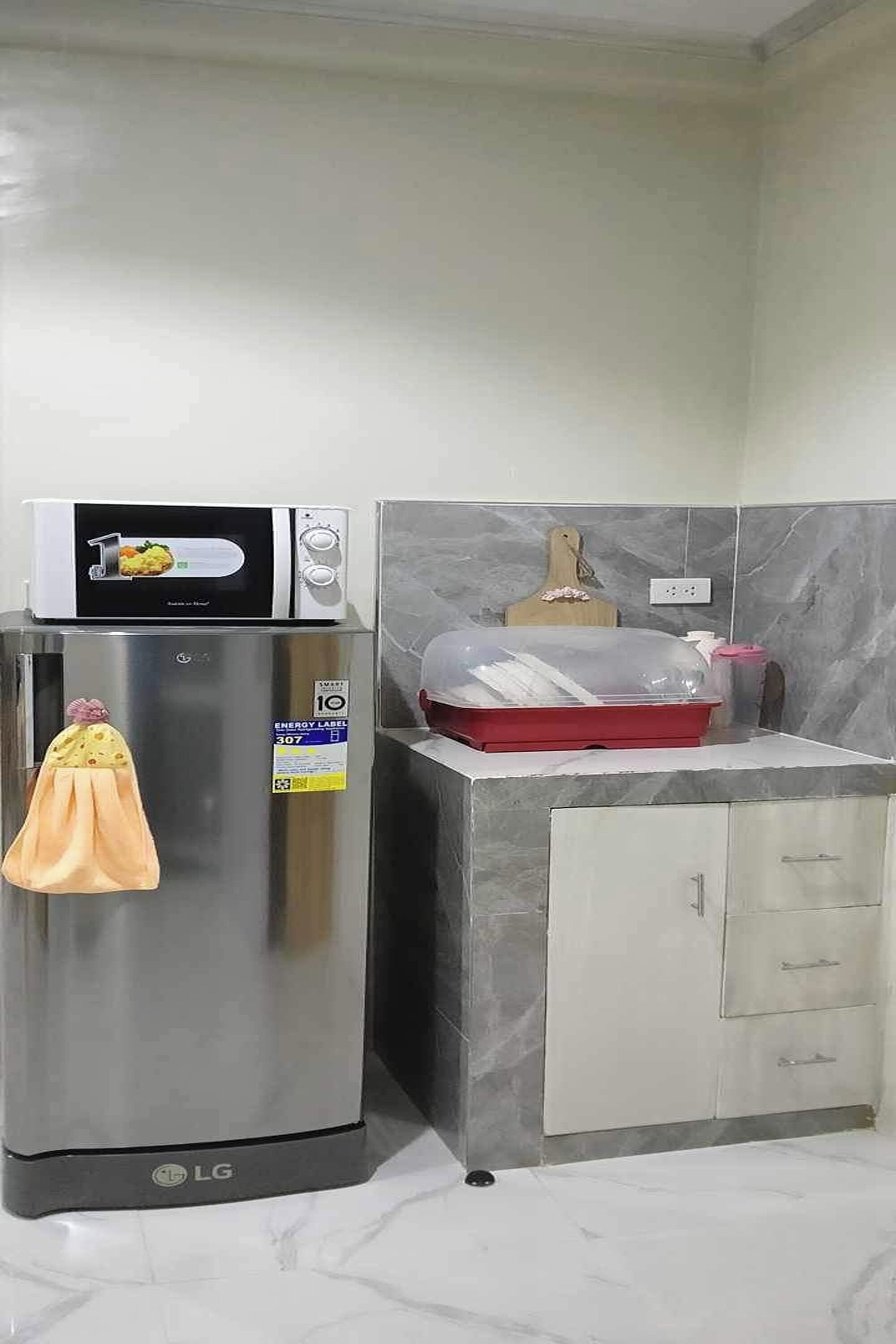 A kitchen with a stainless steel refrigerator, microwave, and a marble countertop.