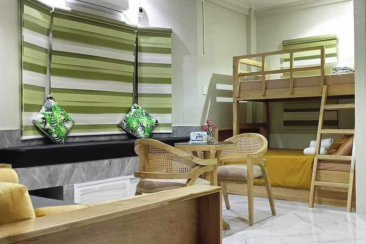 Ein Zimmer mit Etagenbetten, einem kleinen Tisch mit Stühlen und einem Fenster mit Jalousien.