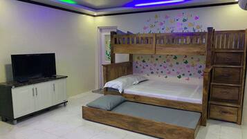 Una cama litera con un televisor sobre un mueble bajo, un aparador de madera y una pared decorada con motivos florales.