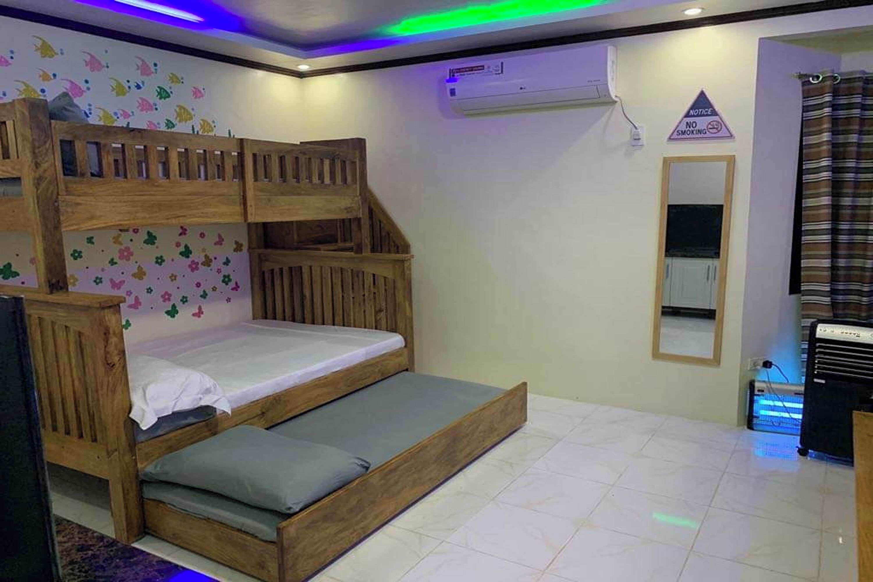 Een stapelbed met houten frame, een wit matras en een grijs kussen. Er is een wandairconditioner en een 'Niet roken' bordje.