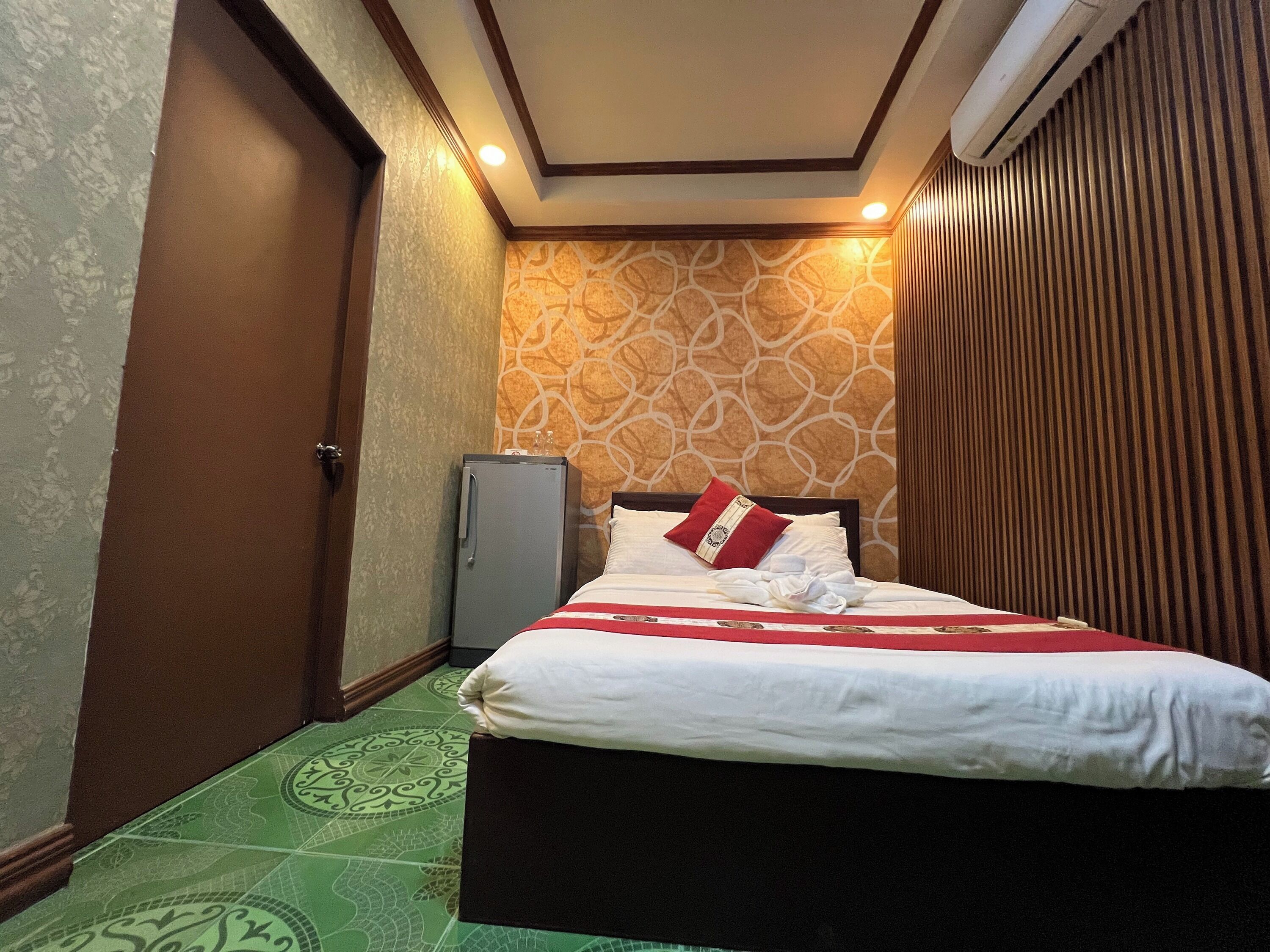 A hotel room with a bed, a small refrigerator, and patterned walls.