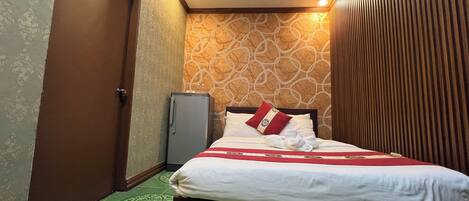 A hotel room with a bed, a small refrigerator, and patterned walls.