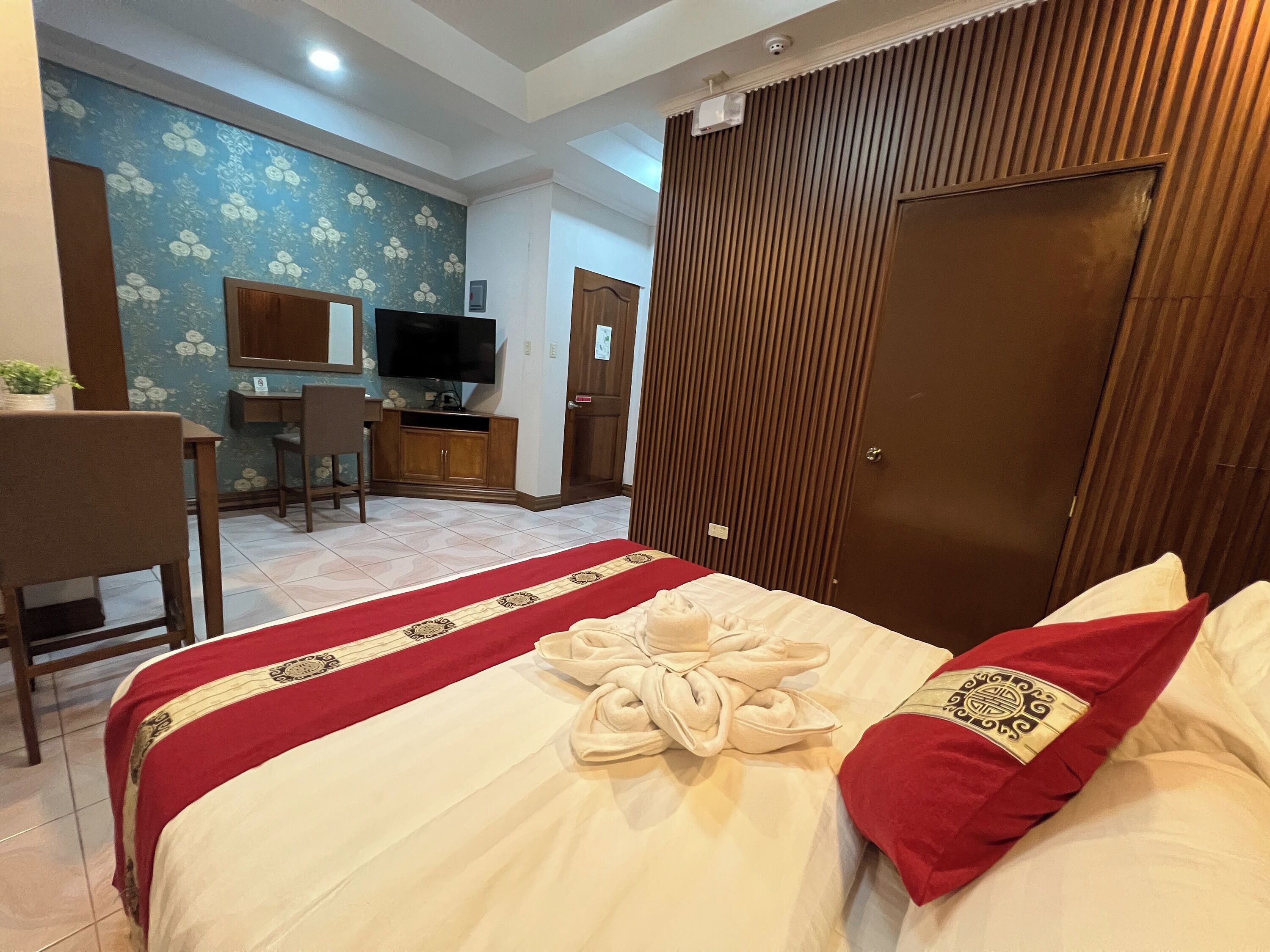 Een hotelkamer met een bed, bureau, televisie en garderobe.