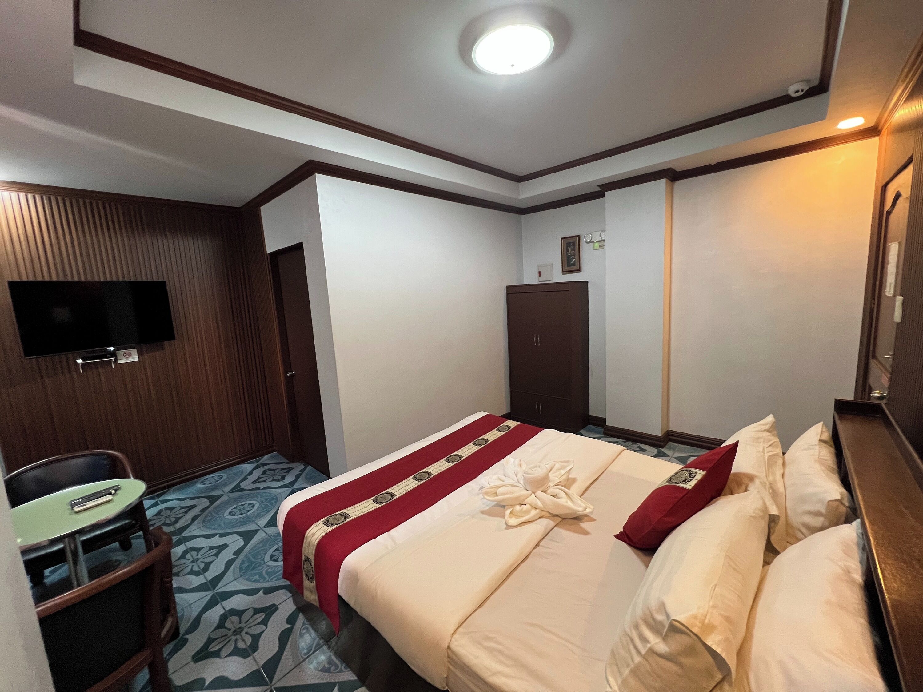 Una habitación de hotel con una cama, un televisor montado en la pared, un escritorio con una silla y un armario.
