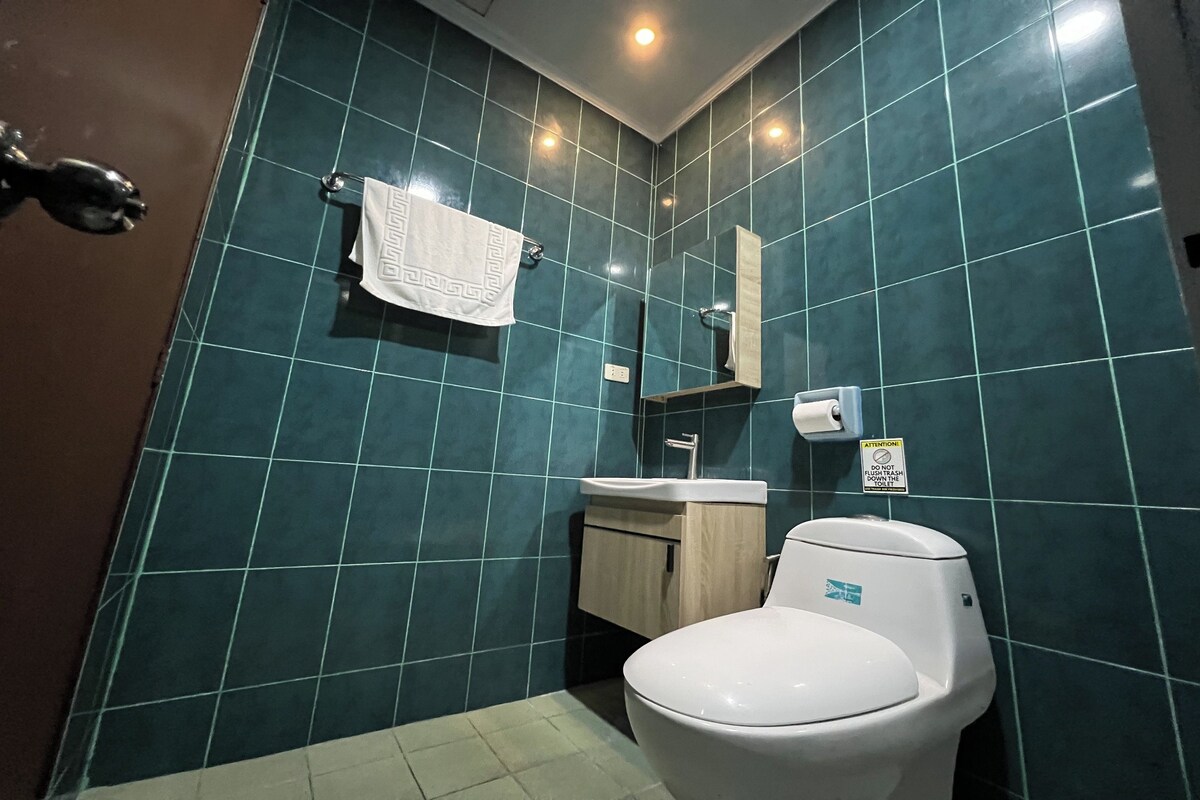 A bathroom with teal tiles, a white toilet, a wooden cabinet, and a mirror.
