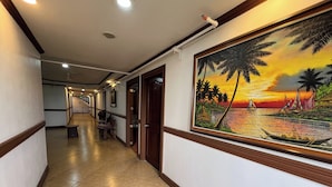 A hallway with a tiled floor, wooden trim, and a large painting of a sunset over water with palm trees. - Rossa Hotel Clark near Airport (Angeles City)