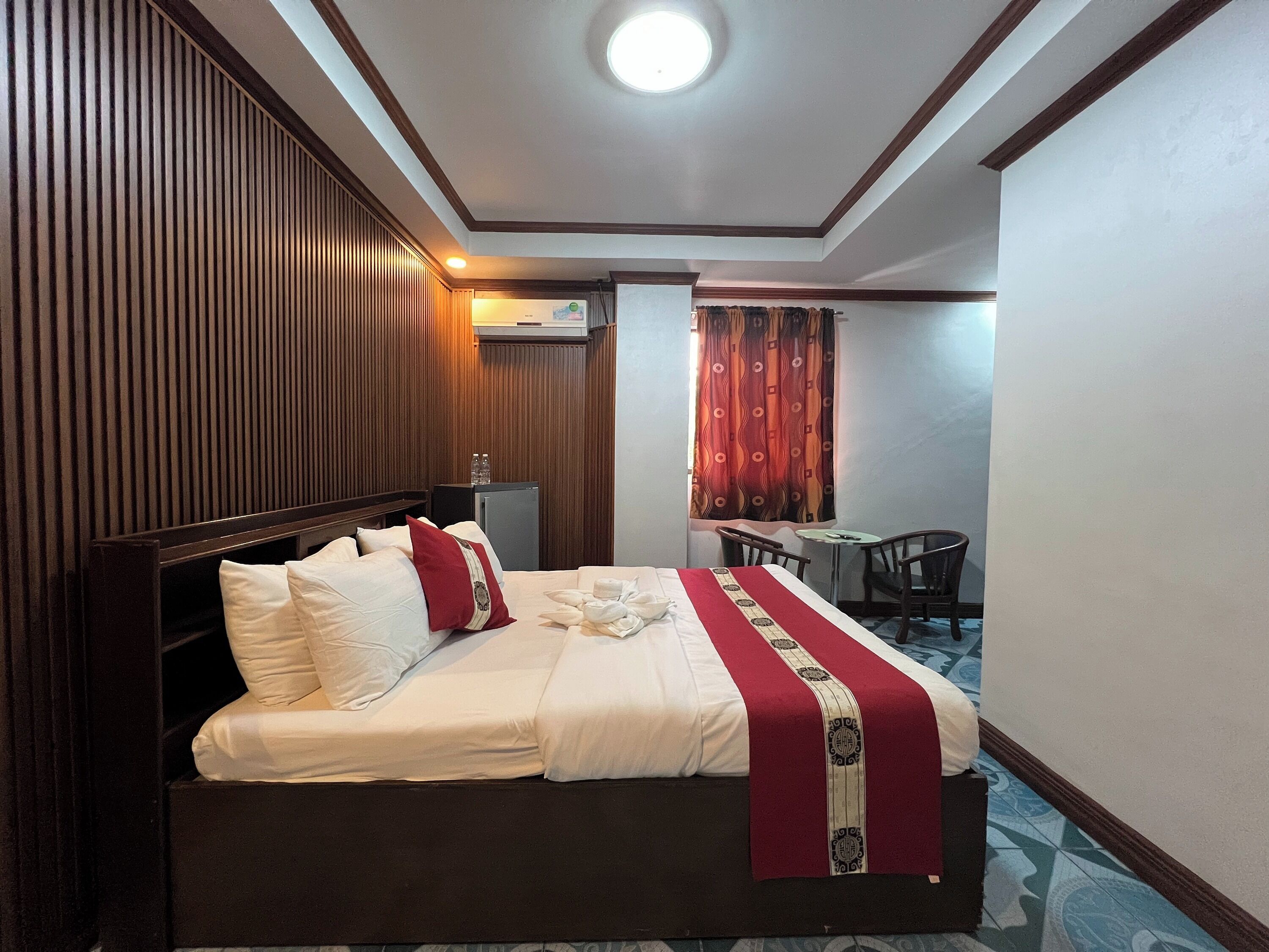 A hotel room with a large bed, a small desk, a chair, and a window with curtains.