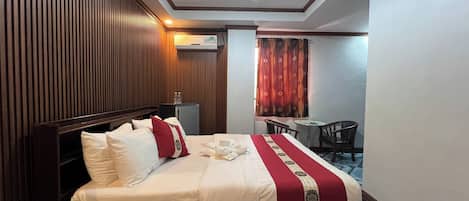 Habitación de hotel con una cama grande, un escritorio pequeño, una silla y una ventana con cortinas.