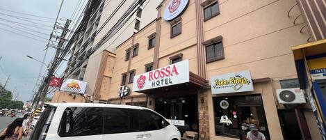 A hotel named ROSSA HOTEL with a signboard, a parked white car, and a motorcycle outside.