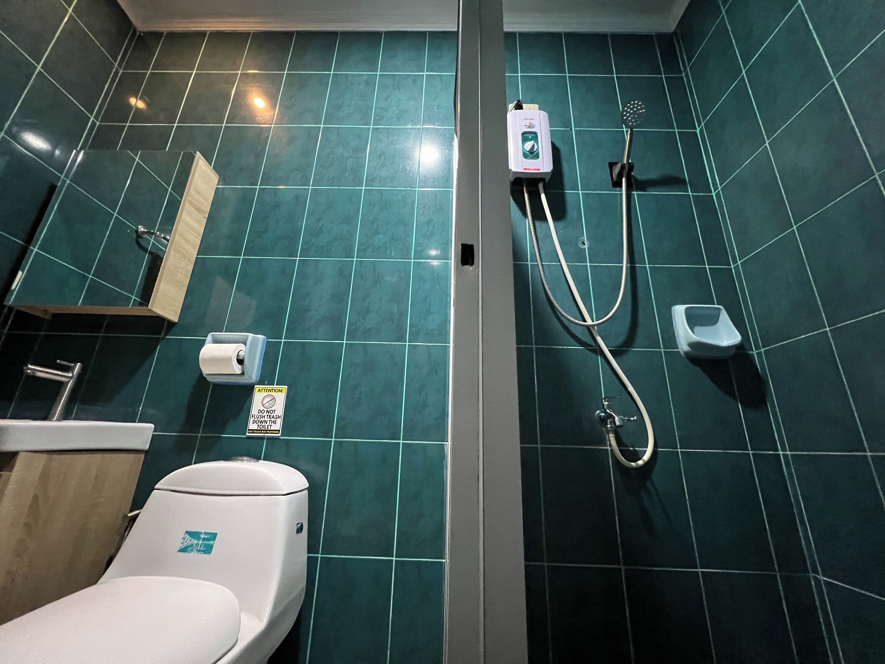 A bathroom with a toilet, a hand dryer, a paper towel dispenser, and a hand soap dispenser.