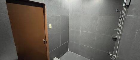A bathroom with dark tiles, a shower, a sink, and a door.