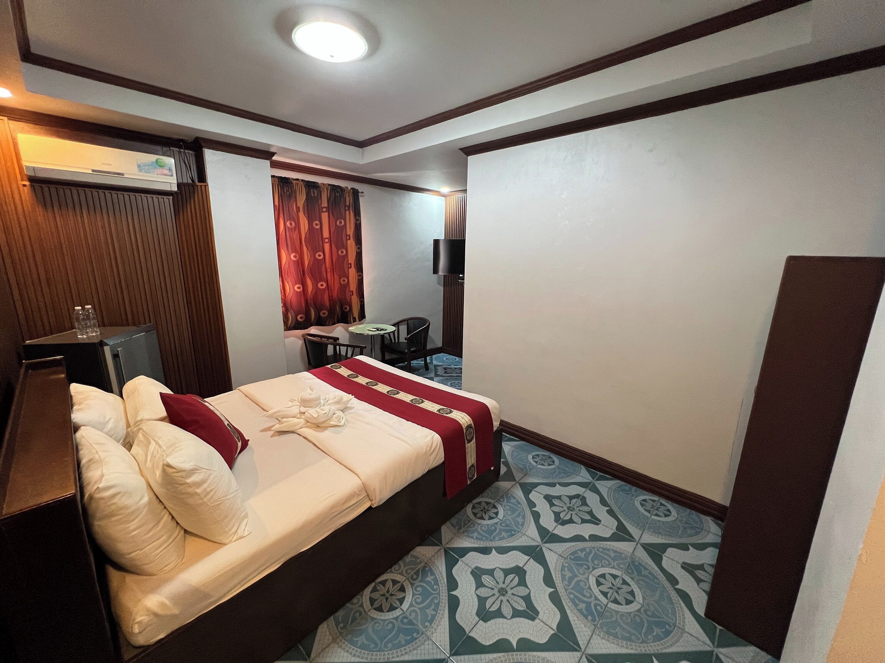 A hotel room with a bed, a desk, a chair, a TV, and a window with curtains.