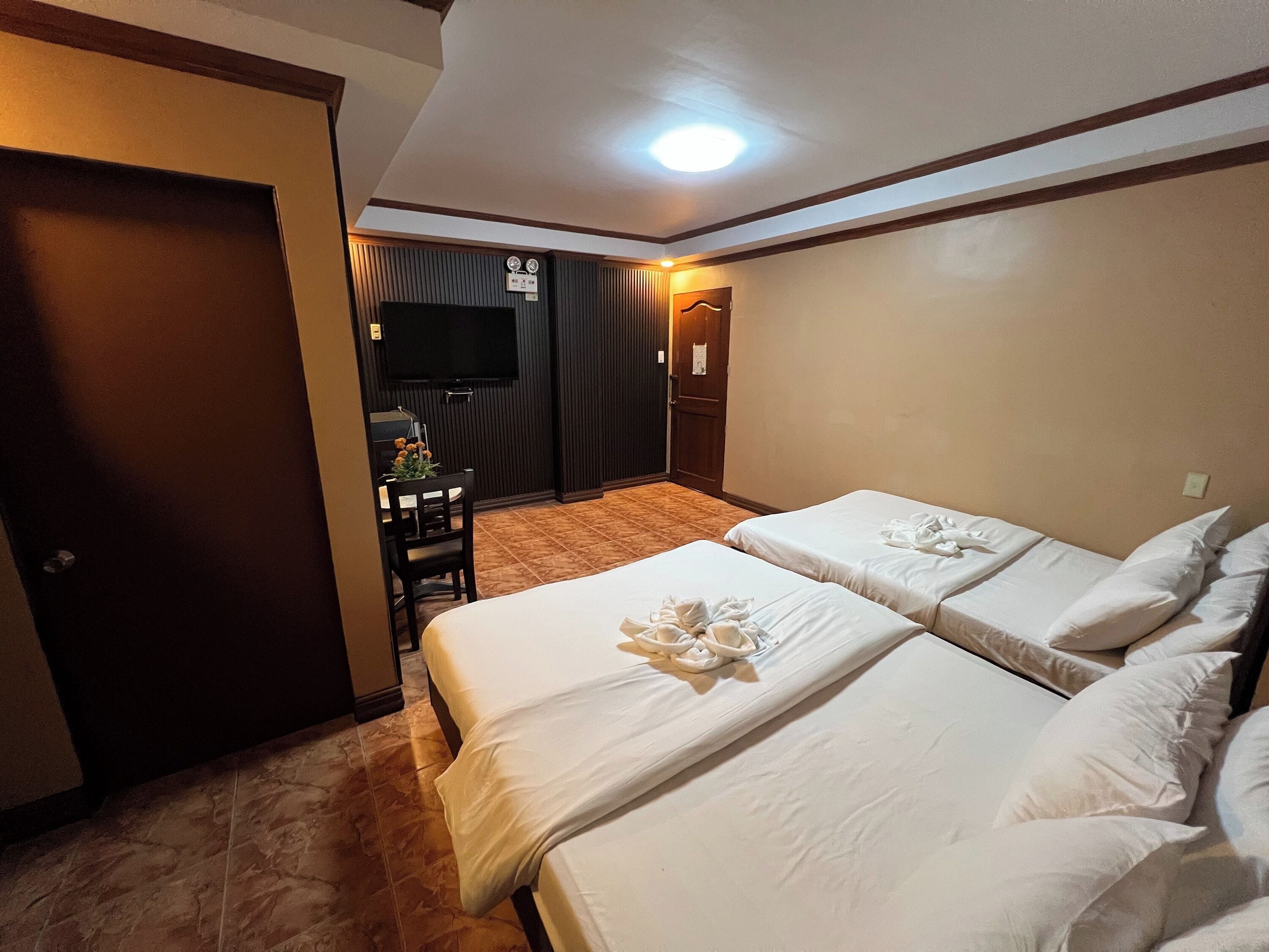 A hotel room with two beds, a television, a desk with a chair, and a door.