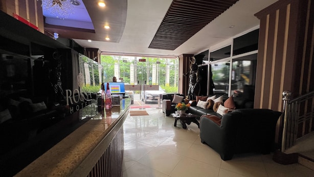 A hotel lobby with a reception desk, a sofa with cushions, a statue, and a large window offering a view of greenery outside. - Rossa Hotel Clark near Airport (Angeles City)