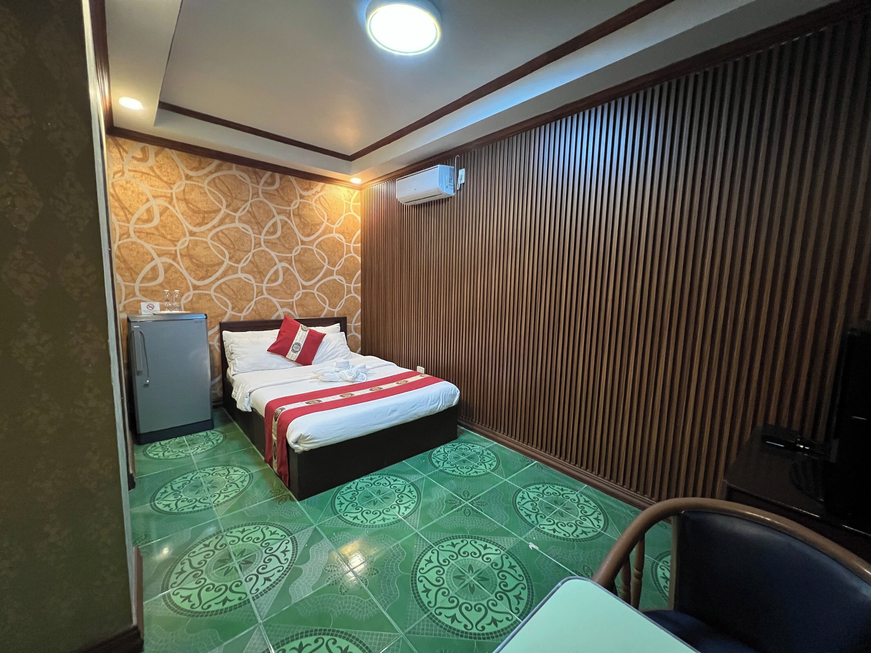 Habitación de hotel con cama, un refrigerador pequeño, pared de paneles de madera y baldosas de suelo con diseños.