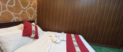 Una habitación de hotel con una cama, un almohadón rojo, un almohadón blanco, una colcha roja y blanca, y un equipo de aire acondicionado en la pared.