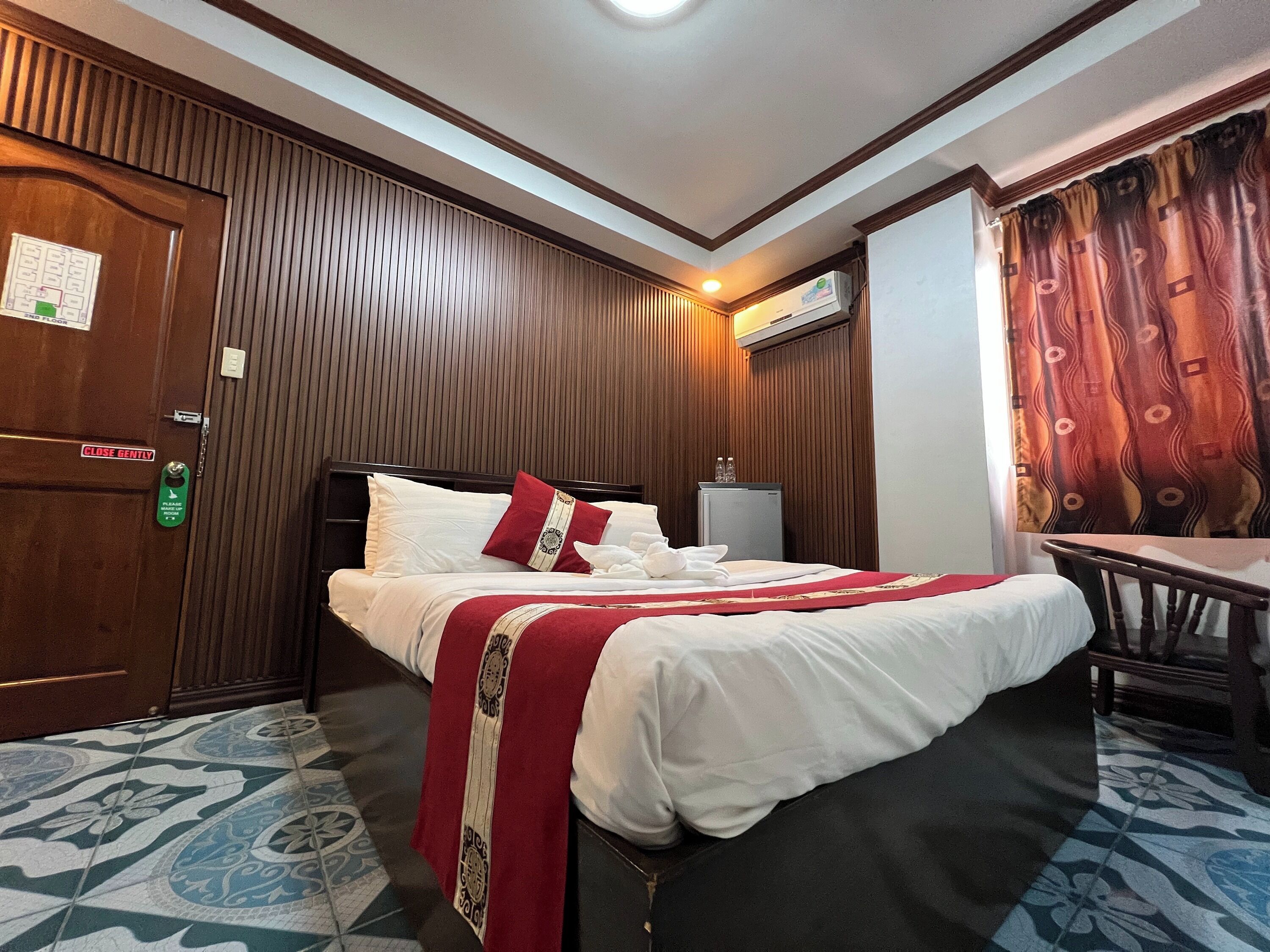 Una habitación de hotel con cama, escritorio, silla, puerta y aire acondicionado.