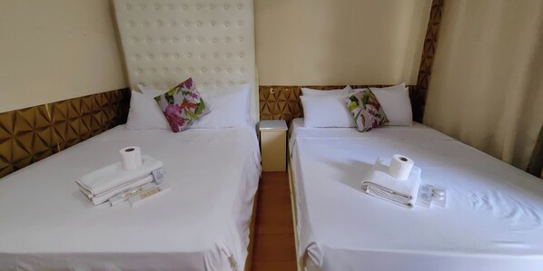 Two twin beds with white linens, each with a pillow and a set of toiletries.