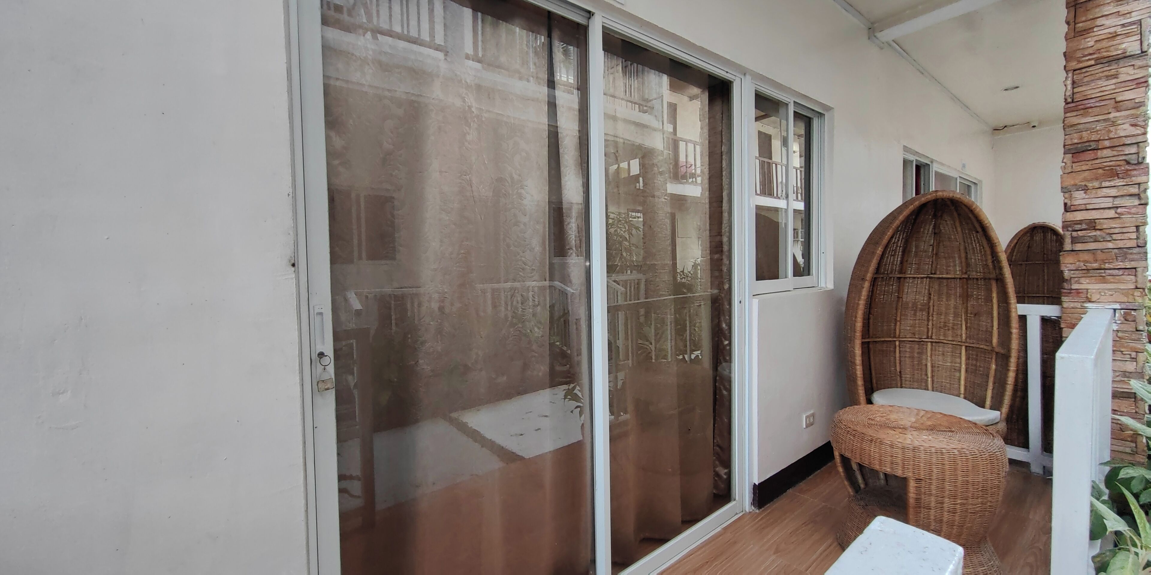 A room with sliding glass doors leading to a balcony, a wicker chair, and a small table.