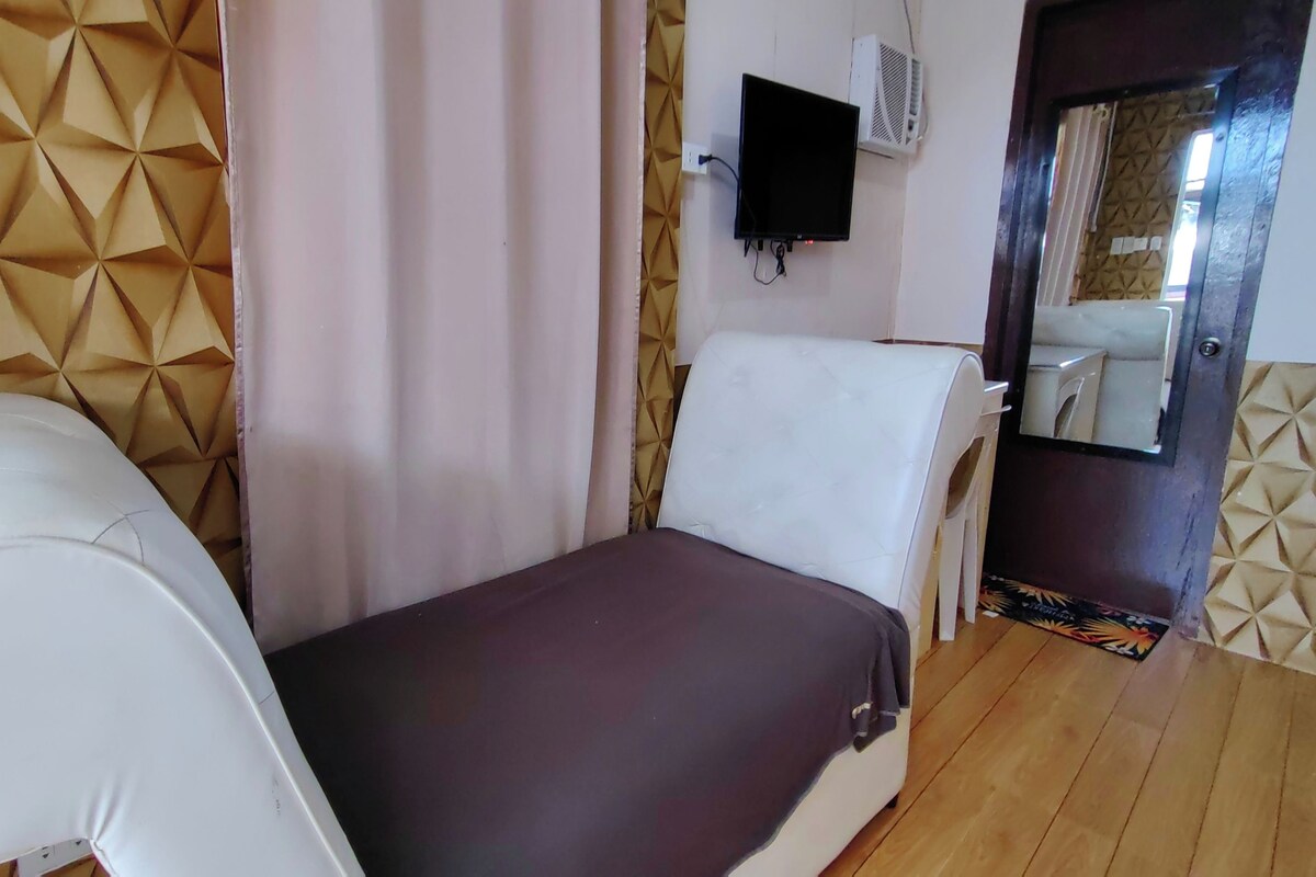 A small, private room with a bed, a chair, a television, and a wall-mounted air conditioner.