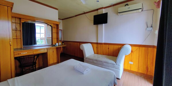 Une chambre d’hôtel équipée d’un bureau en bois, d’une télévision, d’un climatiseur et d’un lit avec un oreiller.