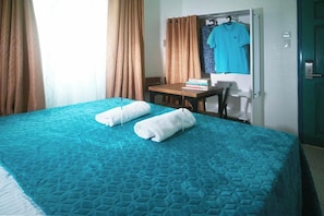 Una habitación de hotel con cama, una mesa, una silla, un ventanal con cortinas y una puerta.