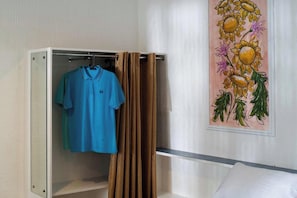 Ein Zimmer mit einem Bett, einem Schrank mit einem darin hängenden blauen Hemd und einem Wandbild mit einem Sonnenblumenmotiv.