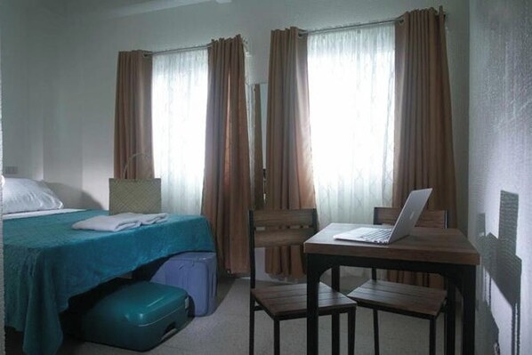 A hotel room with a bed, a desk with a laptop, a chair, a suitcase, and curtains. - 1001 Nights Boutique Inn (Cagayan de Oro)