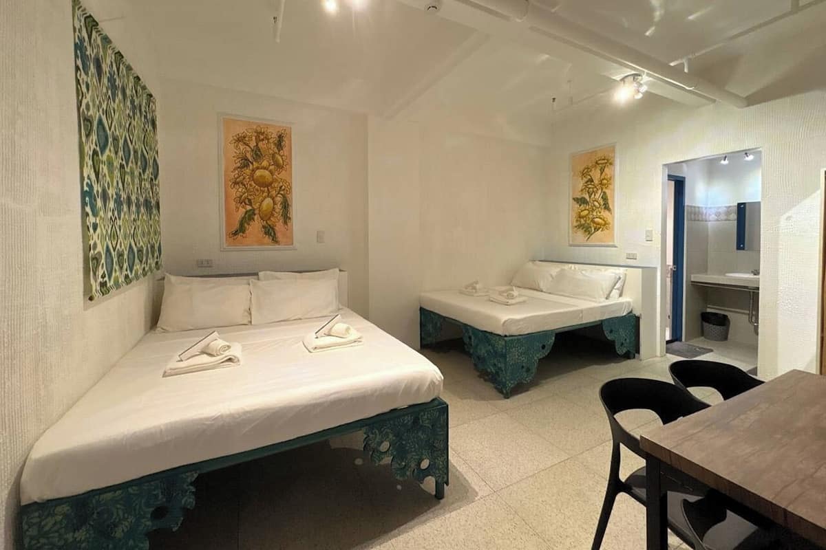 Una camera d'albergo con due letti, un tavolo, sedie e opere d'arte alle pareti.