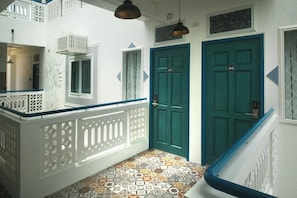 A hallway with patterned floor tiles, a white decorative railing, and two teal doors. - 1001 Nights Boutique Inn (Cagayan de Oro)