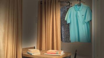 A room with a wooden table, two books, a hanging light blue shirt, and a patterned curtain.