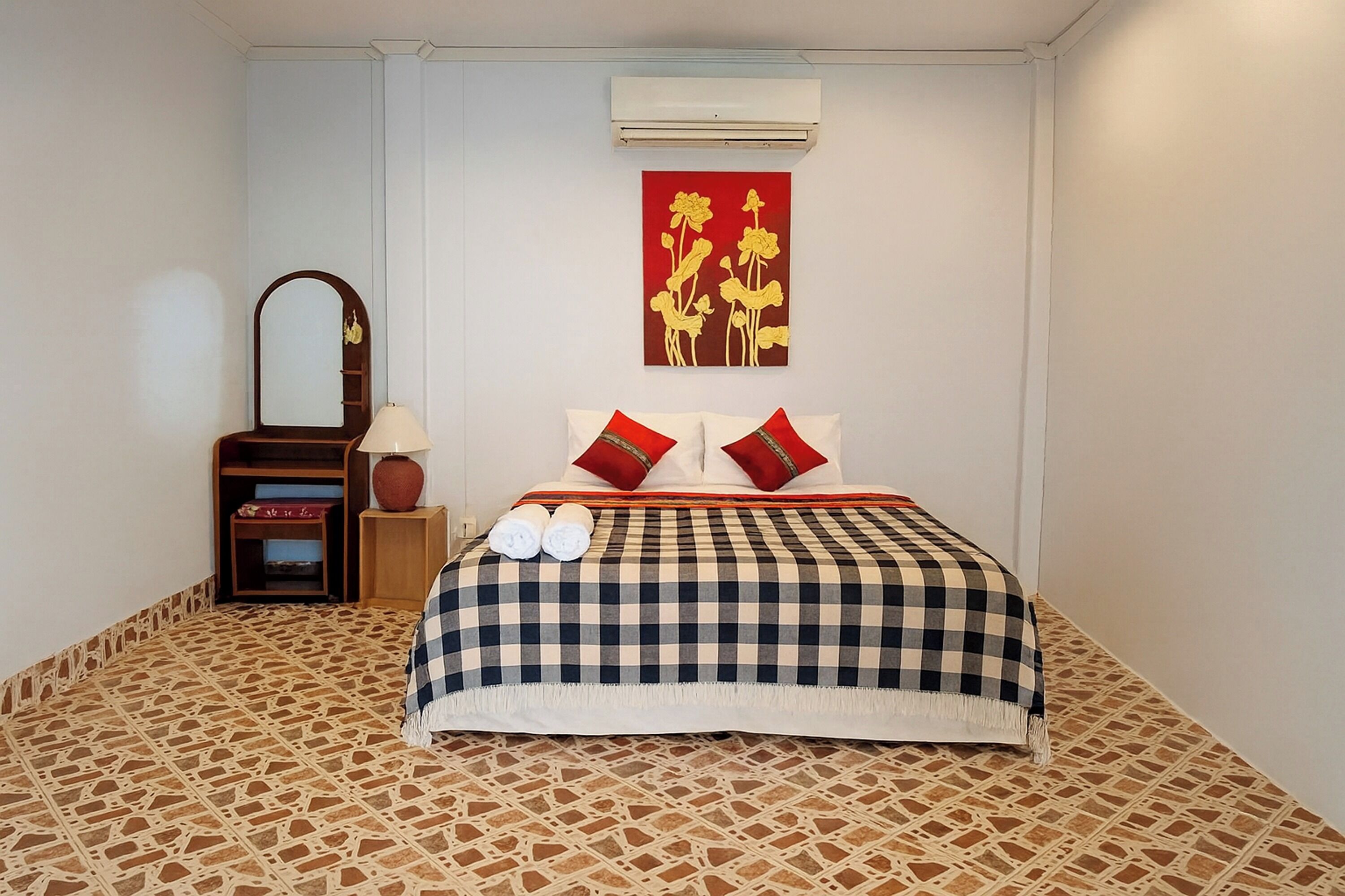 Een netjes ingerichte hotelkamer met een geruit beddegoed, een spiegel, een wandairconditioner en een decoratief schilderij.