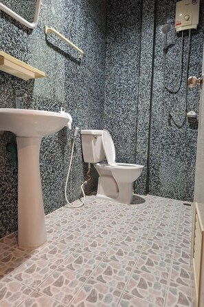 Une salle de bain avec un mur décoré d’un motif imitant le granit, un lavabo sur colonne, des toilettes et un espace douche.