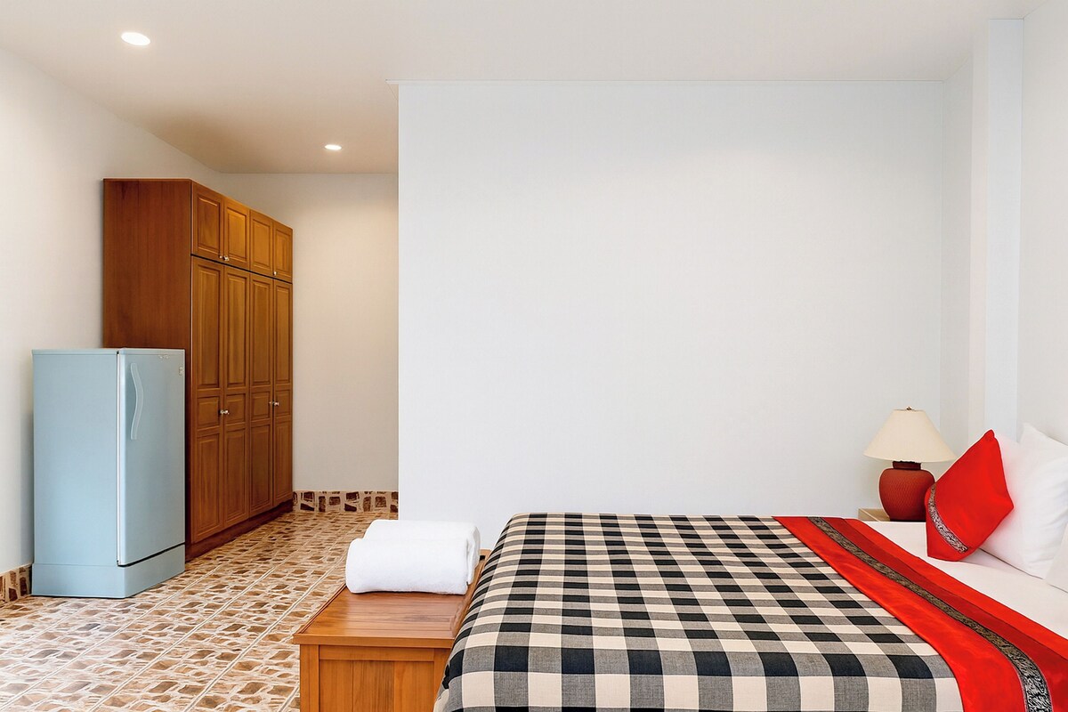 Een hotelkamer met een bed, een houten garderobe, een blauwe koelkast, een nachtkastje met een witte handdoek en een lamp.