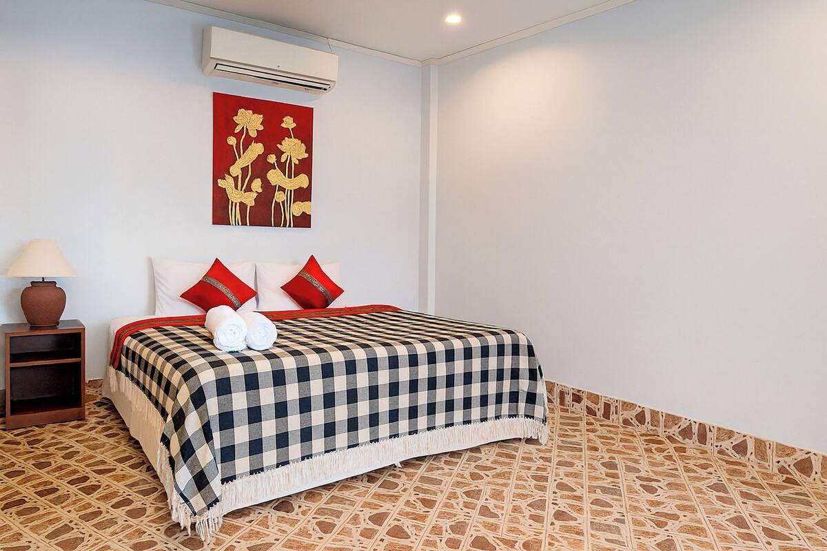 Un lit bien fait, recouvert d’une couvre-lit à carreaux, avec une tapisserie murale rouge et or, et un sol à motifs.