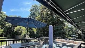 An outdoor deck with a table and chairs, a large umbrella, and a cushioned seating area. - A cozy house with best location (Charlotte)