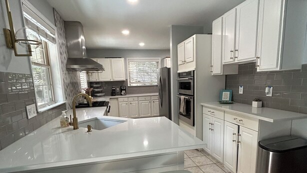 A modern kitchen with white cabinetry, a large island with stools, stainless steel appliances, and a wooden floor. - A cozy house with best location (Charlotte)