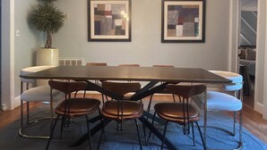 A dining area with a long table, six chairs, two framed abstract paintings, a potted plant, and a chandelier. - A cozy house with best location (Charlotte)