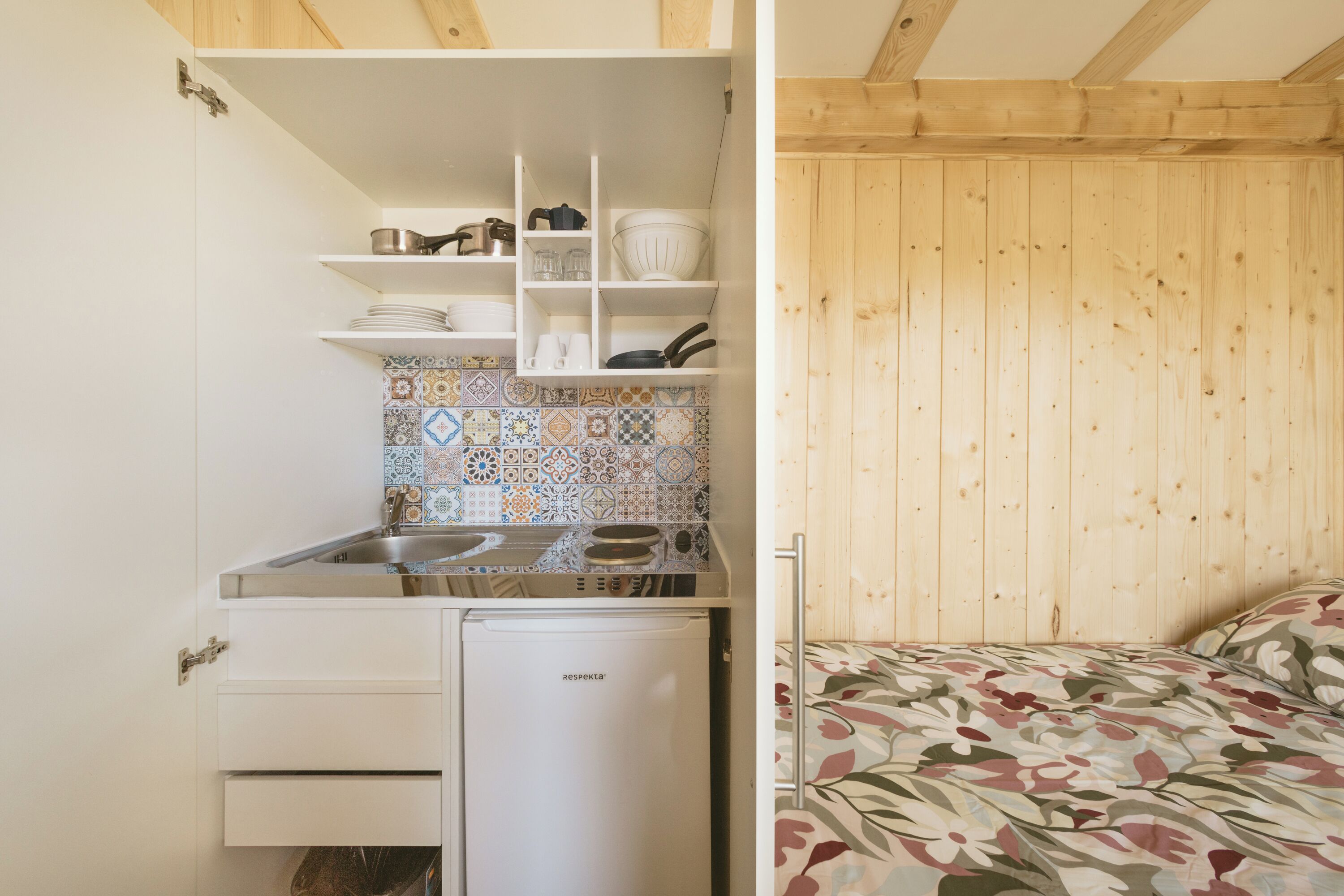 A compact kitchen with a built-in refrigerator, shelves with dishes, and a tiled backsplash.