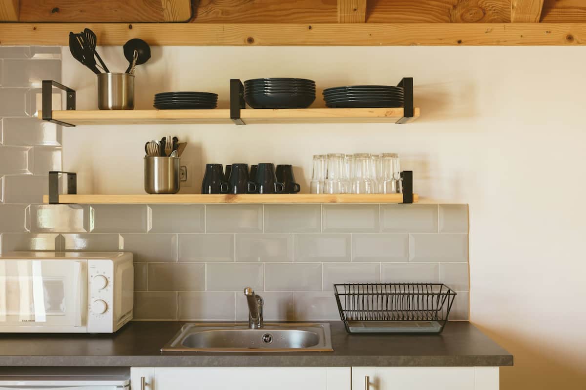 A kitchen with a microwave, toaster, sink, and shelves holding dishes and utensils.