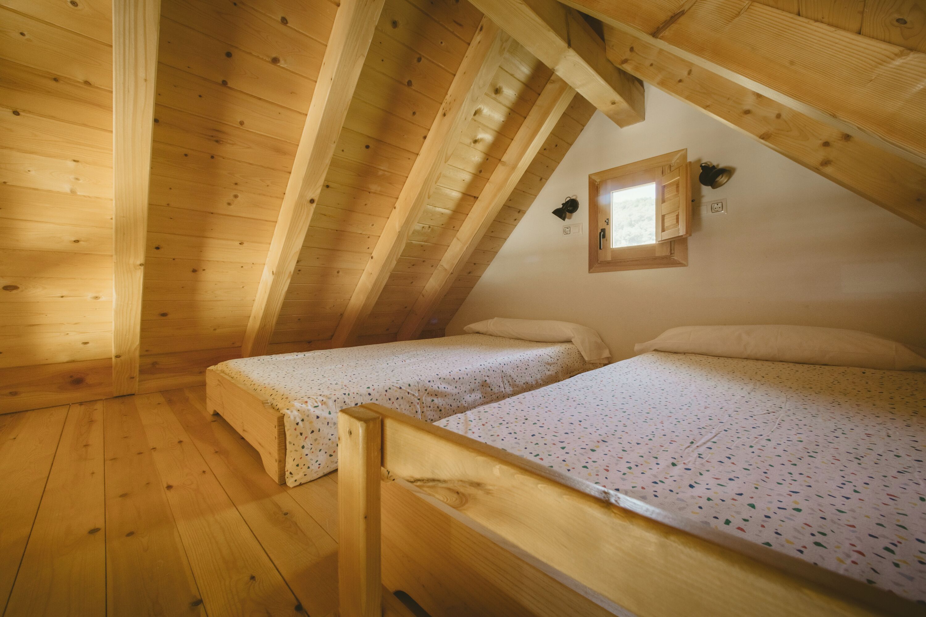 A wooden cabin with two single beds, a small window, and a sloped ceiling.