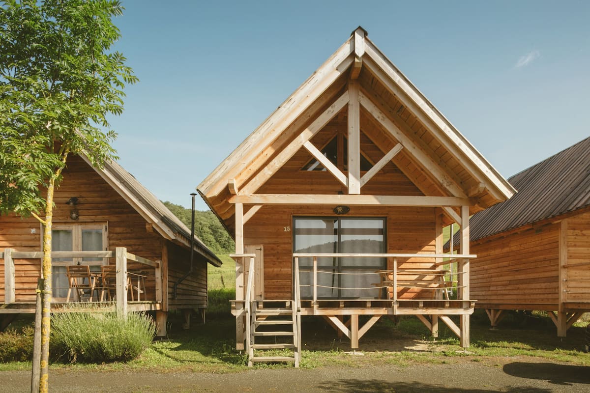 A wooden cabin with a balcony and a window, surrounded by greenery.