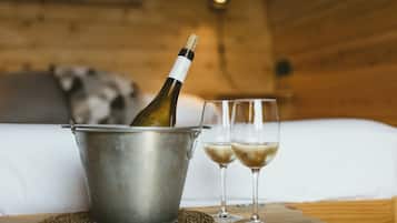 A bottle of champagne in a metal bucket, two glasses of champagne, and a bed in a wooden room.