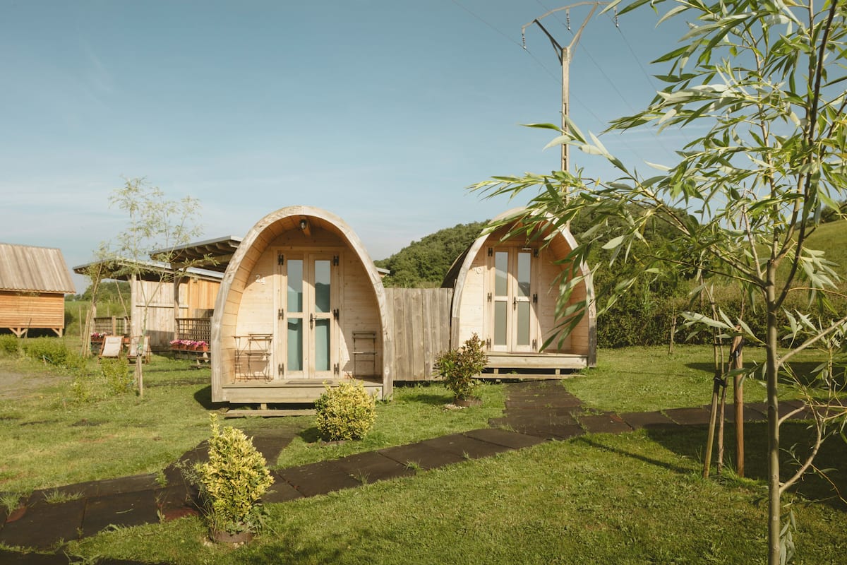 Two small, semi-circular wooden cabins with a single door and window each, surrounded by a grassy area with a small path leading to them.