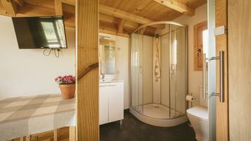 Interior de madera con ducha, inodoro, lavabo y televisor montado en la pared.